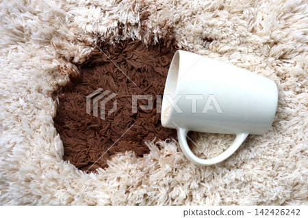 A white coffee mug creating a large brown stain on carpet. 142426242