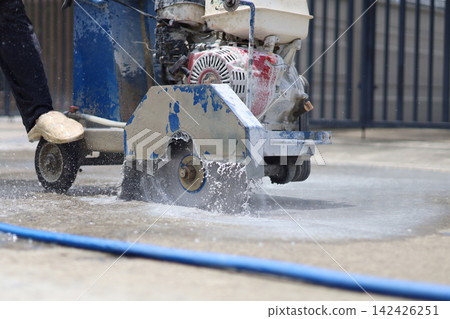 A walk-behind concrete cutter machine, concrete cutter blade spinning with water. A walk-behind concrete cutter machine, concrete cutter blade spinning with water. 142426251