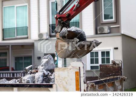 An excavator bucket scooping up broken concrete debris into a dump truck at a road construction site. An excavator bucket scooping up broken concrete debris into a dump truck at a road construction site. 142426319