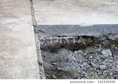 A trench dug into a concrete floor, Road surface under repair showing soil and stones beneath the concrete layer. A trench dug into a concrete floor, Road surface under repair showing soil and stones beneath the concrete layer. 142426499