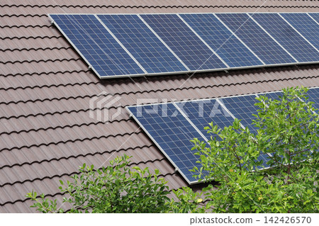 Solar panels installed on a brown tiled roof with green trees 142426570
