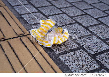 A piece of crumpled yellow and white striped paper garbage littered on a cobblestone sidewalk next to tactical paving. A piece of crumpled yellow and white striped paper garbage littered on a cobblestone sidewalk next to tactical paving. 142426573