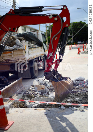 An excavator bucket scooping up broken concrete debris into a dump truck at a road construction site. An excavator bucket scooping up broken concrete debris into a dump truck at a road construction site. 142426621
