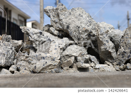 Ruined concrete pile and debris on the ground with a blurry residential background. Ruined concrete pile and debris on the ground with a blurry residential background. 142426641