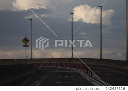 蜿蜒的道路、路燈和陰雲密佈的天空。 142427826