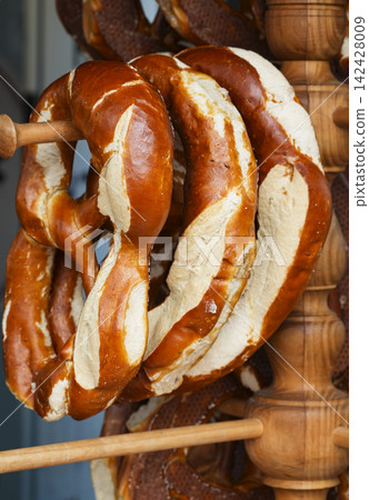 Fresh baked pretzels hanging on a wooden rack in a bakery, illustrating a rustic wooden pretzel stand. Fresh baked pretzels hanging on a wooden rack in a bakery, illustrating a rustic wooden pretzel stand. 142428009