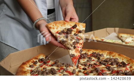 Hands hold a delicious slice of pizza with meat, mushrooms, and cheese, pulled from a cardboard box. The atmosphere is cozy, like a beef pizza lunch or dinner. Hands hold a delicious slice of pizza with meat, mushrooms, and cheese, pulled from a cardboard box. The atmosphere is cozy, like a beef pizza lunch or dinner. 142428639
