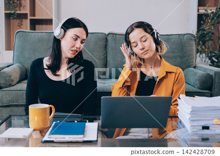 Two young female students using a laptop while sitting on a sofa at home. Student life concept with studying, teamwork, and online learning. Two young female students using a laptop while sitting on a sofa at home. Student life concept with studying, teamwork, and online learning. 142428709