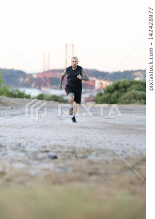 Runner on a dirt path near a bridge in Lisbon during sunset Runner on a dirt path near a bridge in Lisbon during sunset 142428977