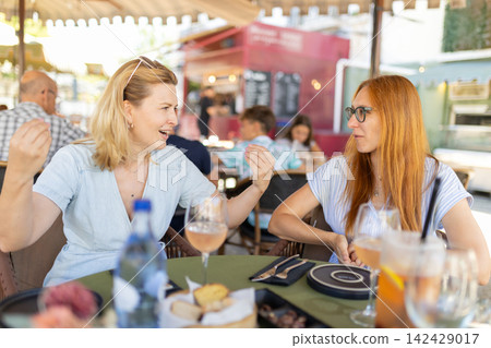 Friends talk and share moments at a cafe during a sunny day in a busy outdoor setting with food and drinks present Friends talk and share moments at a cafe during a sunny day in a busy outdoor setting with food and drinks present 142429017