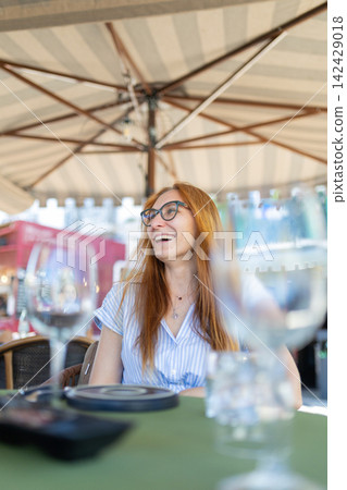 Woman sitting at a cafe table enjoying conversation under an umbrella Woman sitting at a cafe table enjoying conversation under an umbrella 142429018