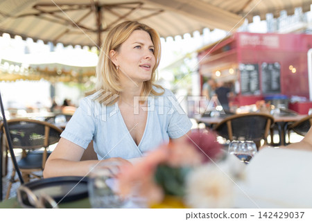Woman sits at outdoor cafe during daytime in a busy market area Woman sits at outdoor cafe during daytime in a busy market area 142429037