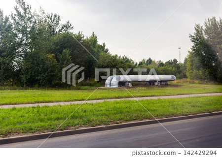 Long industrial pipeline aboveground crossing grassy roadside under cloudy sky with trees in background and paved road in foreground, with pipeline, industrial, infrastructure, gasline detail Long industrial pipeline aboveground crossing grassy roadside under cloudy sky with trees in background and paved road in foreground, with pipeline, industrial, infrastructure, gasline detail 142429294