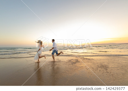 Couple runs on the beach at sunset, enjoying the warm water and soft sand, creating memories together 142429377