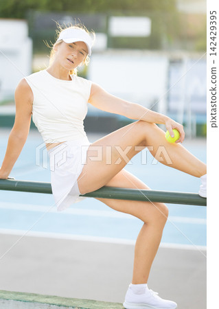 Woman tennis player resting on court fence Woman tennis player resting on court fence 142429395