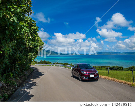 A rental car driving along the coastal road of Ishigaki Island under a blue sky – an image of a summer trip to Okinawa. A rental car driving along the coastal road of Ishigaki Island under a blue sky – an image of a summer trip to Okinawa. 142429515