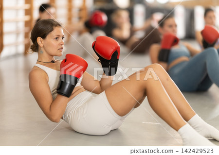Girls in boxing gloves are sitting on floor, doing abdominal exercise and working with hands Girls in boxing gloves are sitting on floor, doing abdominal exercise and working with hands 142429523