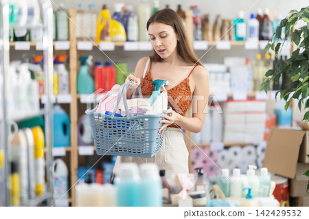 Girl selects various household cleaning products for cleaning the house with full basket of various purchases Girl selects various household cleaning products for cleaning the house with full basket of various purchases 142429532