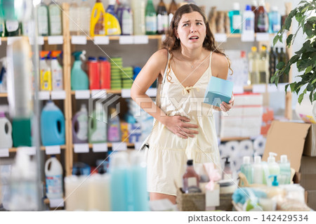 Young woman suffers from abdominal pain, feels pain in her stomach, while visiting household goods supermarket Young woman suffers from abdominal pain, feels pain in her stomach, while visiting household goods supermarket 142429534