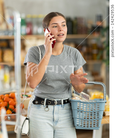 Young woman choosing groceries while talking on phone Young woman choosing groceries while talking on phone 142429536