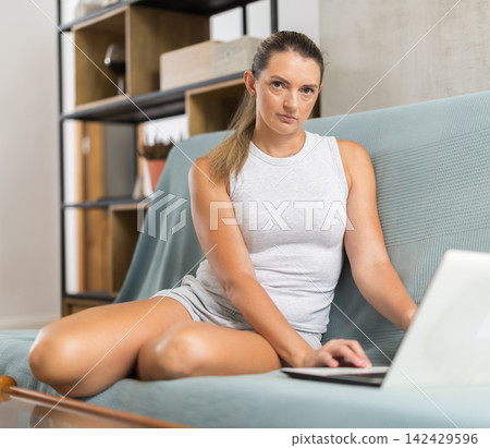 Adult woman working on laptop sitting on sofa 142429596