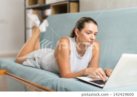 Woman working on computer and sitting on sofa Woman working on computer and sitting on sofa 142429600