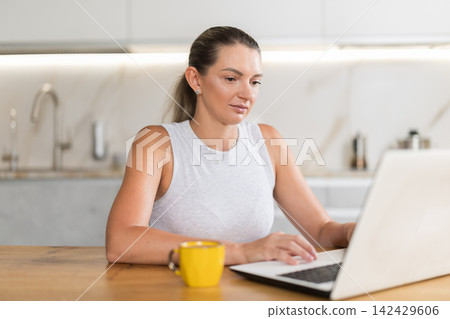 Adult woman working on laptop in kitchen Adult woman working on laptop in kitchen 142429606