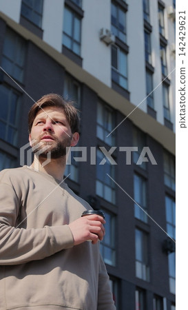 Vertical video. Portrait of a young man holding a paper cup in front of modern buildings. Vertical video. Portrait of a young man holding a paper cup in front of modern buildings. 142429621
