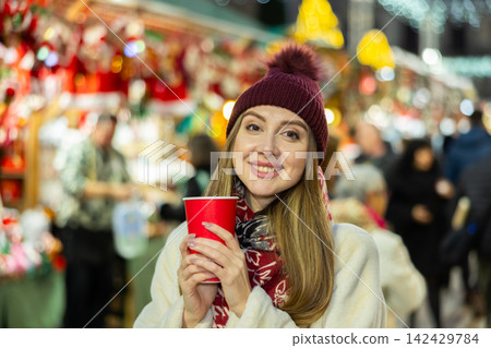 Young woman stands with glass of hot coffee in her hands and enjoys festive New Year atmosphere Young woman stands with glass of hot coffee in her hands and enjoys festive New Year atmosphere 142429784