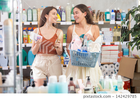 Two girls friends buyers with filled basket household chemistry wanders around store, looking at display cases 142429785