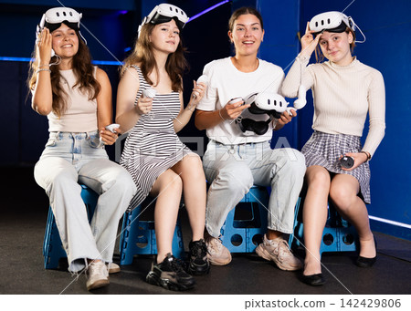 Cheerful teenage girls sitting in virtual reality game room Cheerful teenage girls sitting in virtual reality game room 142429806