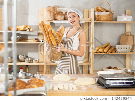 Female baker holding freshly baked baguettes in bakery Female baker holding freshly baked baguettes in bakery 142429844