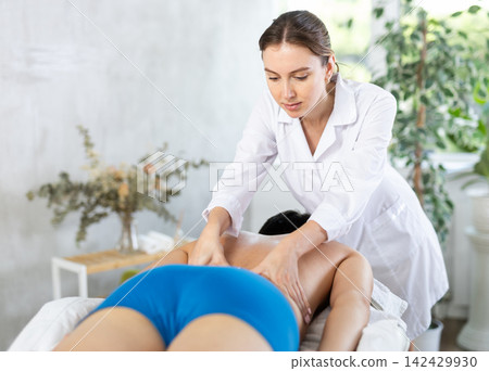Physiotherapist girl actively massages deep muscles along spine to male client Physiotherapist girl actively massages deep muscles along spine to male client 142429930