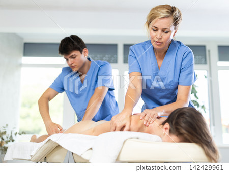 Professional masseur and masseuse performing back massage for female patient Professional masseur and masseuse performing back massage for female patient 142429961