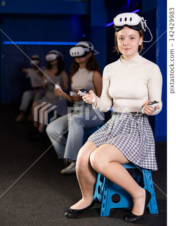Girl gamer with virtual reality glasses on her forehead expresses enthusiastic emotions from playing with her friends in dark room Girl gamer with virtual reality glasses on her forehead expresses enthusiastic emotions from playing with her friends in dark room 142429983