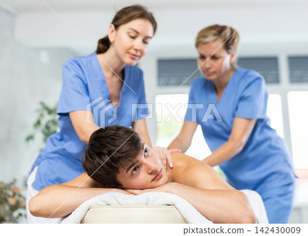 Female professional physiotherapist helps girl student to perform back massage to male client. 142430009