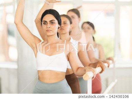Young girl practicing third arm position holding by ballet barre Young girl practicing third arm position holding by ballet barre 142430106