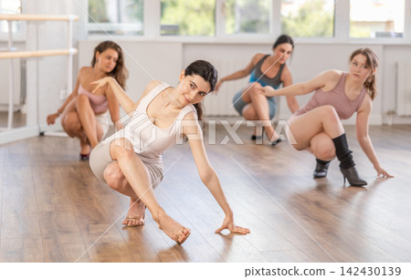 Girls perform dance in heels, squat down, actively repeat movements of instructor. 142430139