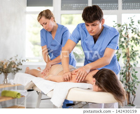 Back massage in four hands simultaneously - two professional masseurs treating woman Back massage in four hands simultaneously - two professional masseurs treating woman 142430159