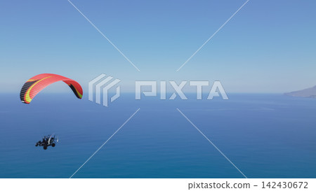 Paraglider soaring above the Aegean Sea in Crete, Greece, with a colorful canopy and a clear blue sky, showcasing the beauty of aerial adventure sports in a coastal landscape Paraglider soaring above the Aegean Sea in Crete, Greece, with a colorful canopy and a clear blue sky, showcasing the beauty of aerial adventure sports in a coastal landscape 142430672
