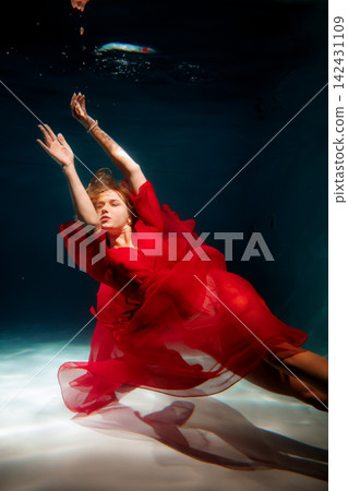 Woman in crimson attire dances gracefully beneath water surface Woman in crimson attire dances gracefully beneath water surface 142431109