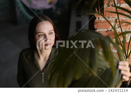 Contemplative female among lush houseplants in daylight Contemplative female among lush houseplants in daylight 142431214