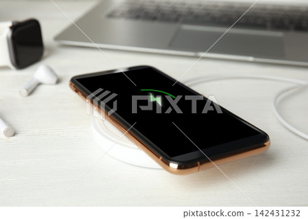 Mobile phone charging with wireless device on white wooden table, closeup 142431232