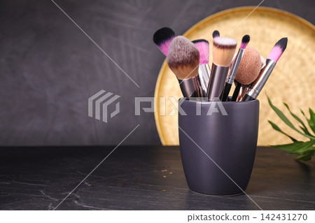 Set of professional makeup brushes in holder on black table. Space for text Set of professional makeup brushes in holder on black table. Space for text 142431270