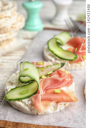 Puffed rice cakes with prosciutto and cucumber on wooden board, closeup 142431486