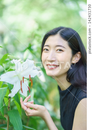 一位二十多歲的日本女子在夏日花園的白色百合花旁微笑。 142431730