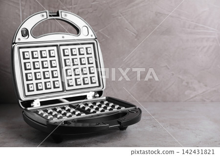 Modern waffle iron on grey stone table. Space for text Modern waffle iron on grey stone table. Space for text 142431821