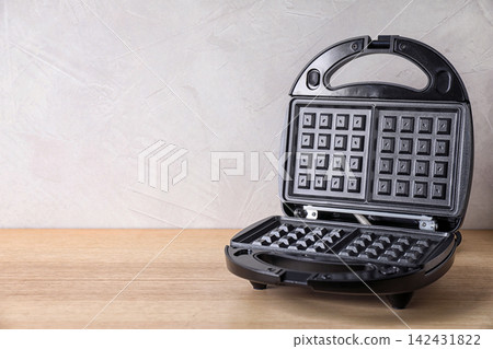 Modern waffle iron on wooden table against white background. Space for text 142431822