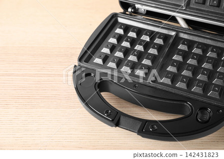 Modern waffle iron on wooden table, closeup Modern waffle iron on wooden table, closeup 142431823