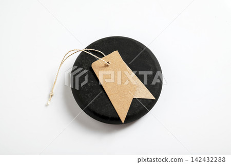 Top view of a round black stone with a blank brown kraft paper tag and string on a white background, ideal for minimalist branding mockups. Mockup or Copyspace Top view of a round black stone with a blank brown kraft paper tag and string on a white background, ideal for minimalist branding mockups. Mockup or Copyspace 142432288